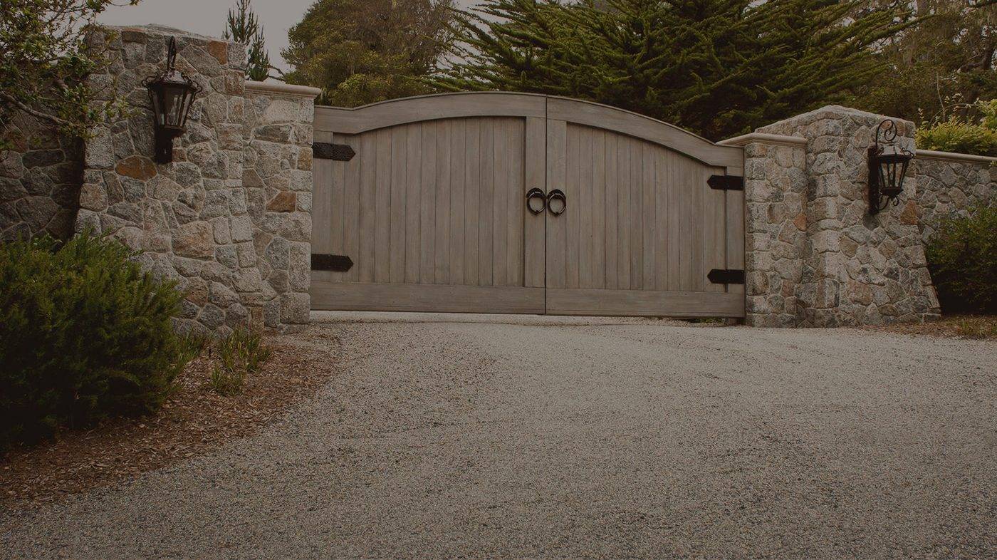 Wooden driveway gate built by Frontier Fence, set between stone pillars